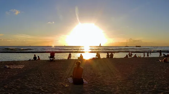Beachgoers and sailboats at sunset on Waikīkī Beach.