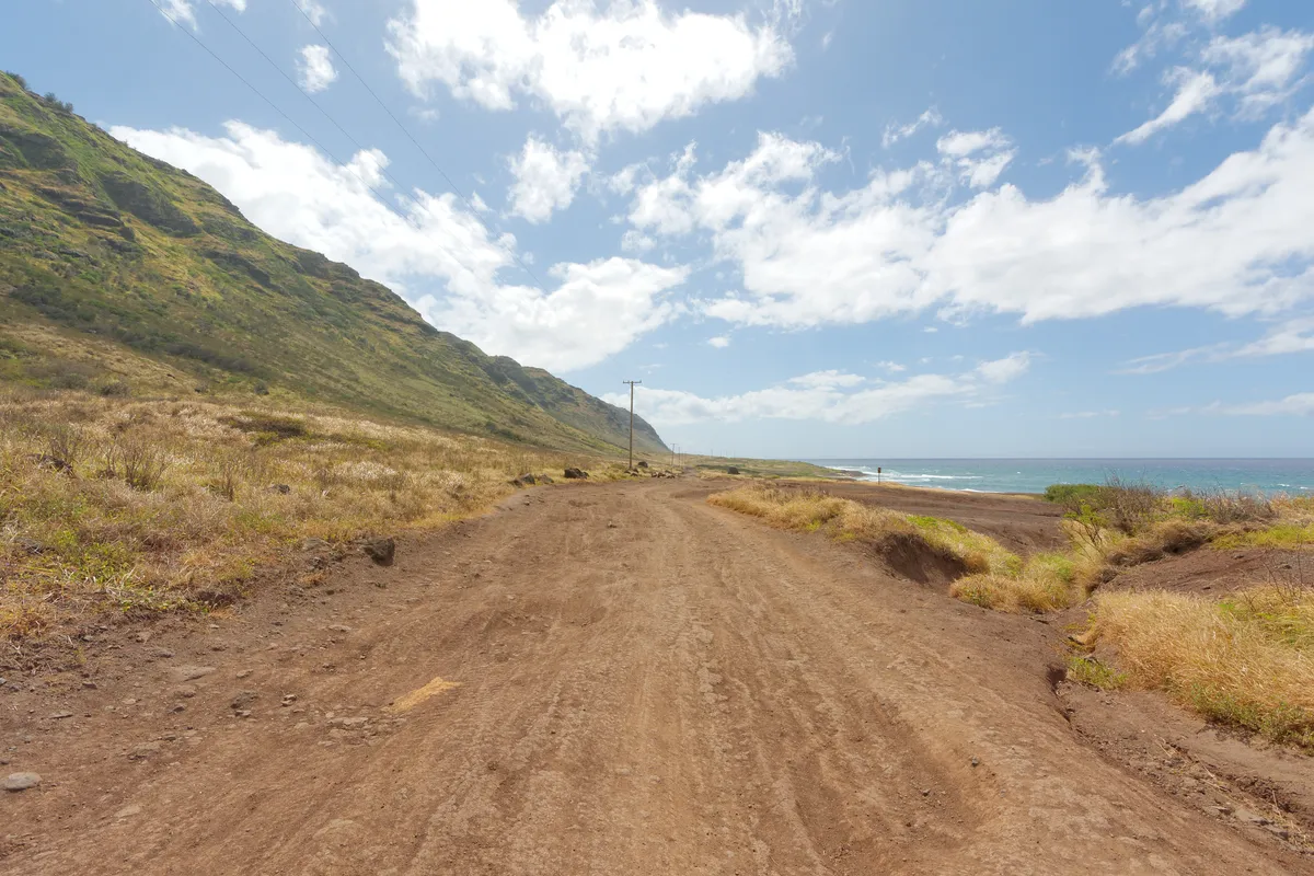 The coastal dirt road toward Kaʻena Point on the Mokulēʻia side, with mountains to the left and ocean to the right.