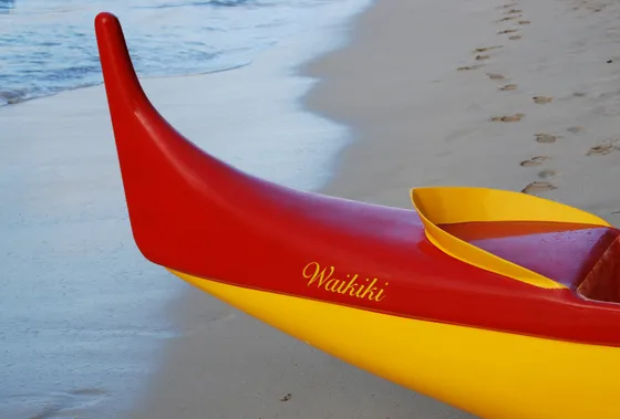 A red and yellow canoe resting on the sand at Waikīkī.