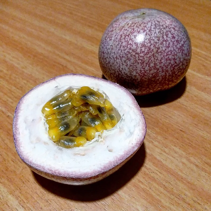 A whole passion fruit beside a cut half showing the seeds.