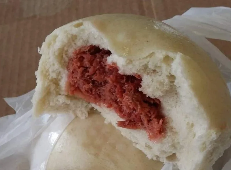 An opened steamed manapua showing its char siu filling.