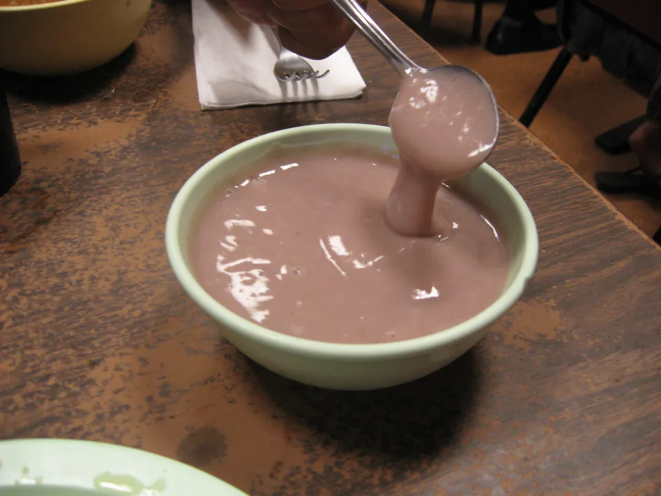 A spoon lifting thick purple poi from a pale green bowl.