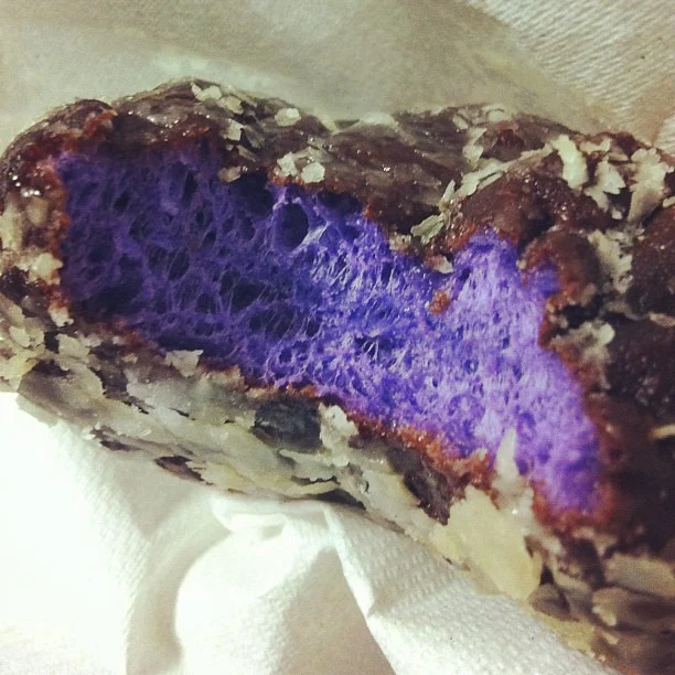 An opened poi donut showing its purple crumb beneath the glaze.