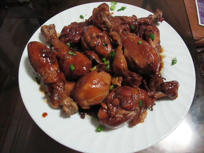 Soy-sauce chicken drumsticks with green onions on a white plate.